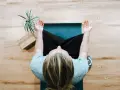Person mediterar på en yogamatta, en grön växt och träblock bredvid. Perfekt för avkoppling på arbetsplatsen.