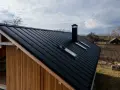 Nowoczesny dom z drewnianą elewacją i czarnym, metalowym dachem dwuspadowym. Idealne rozwiązanie, czym pokryć dach dwuspadowy.