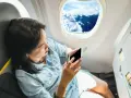 Kobieta z telefonem siedzi przy oknie w samolocie Ryanair, podziwiając chmury.
