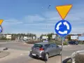 Rondo z tablicami "ustąp pierwszeństwa" i "ruch okrężny". Kierowca w szarym samochodzie może dostać mandat za wymuszenie pierwszeństwa.