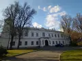 Pałac w Falentach, biała, okazała budowla z wieżyczką, otoczona drzewami o nagich gałęziach, pod błękitnym niebem z chmurami.