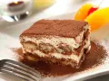 Pyszne tiramisu Ani Starmach, posypane kakao, z owocami i wisienką. Idealne na deser.
