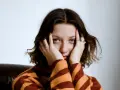 Justyna Święs Piernikowski w swetrze w pasy, z dłońmi przy twarzy, patrzy w obiektyw.