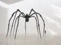 Une araignée monumentale, œuvre d'un artiste contemporain, domine une salle d'exposition. Une silhouette humaine, petite, contemple cette sculpture imposante.