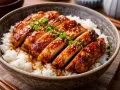 En skål med fluffigt ris toppad med saftig, glaserad teriyaki kyckling, strödd med sesamfrön och grön lök. En utsökt måltid.