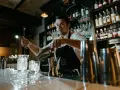 Barman przygotowuje drinki, pokazując, jak założyć drink bar. Na półkach stoją butelki alkoholi.