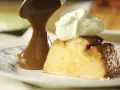 Un trozo de flan de 12 huevos, cubierto con caramelo y crema batida, servido en un plato con diseño azul.