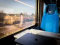 Podróż pociągiem z Katowic do Krakowa Balic. Widok z okna na krajobraz, obok niebieskie siedzenie i stolik z laptopem.