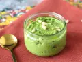 Frisches Rucola Pesto in einem Glas, garniert mit Pinienkernen. Daneben eine goldene Löffel.
