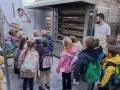 Dzieci z plecakami oglądają piec piekarniczy i półki z chlebem.