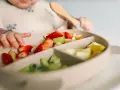 Bebé explorando fresas, kiwi y plátano en su plato. Es un buen momento para ofrecer fruta a los bebés.