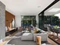Elegante salón con chimenea de piedra, pared de madera y grandes ventanales que conectan con una terraza. Un ejemplo de las últimas tendencias interiorismo.