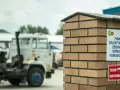 Tablica informuje, co to jest pszok – punkt selektywnego zbierania odpadów komunalnych. W tle widać ciężarówki.