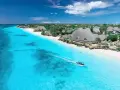 Zanzibar w lutym: idealna pogoda na rajskie wakacje. Turkusowa woda, biały piasek i łódź sunąca po oceanie.