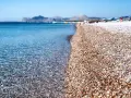 Rodos: turkusowe morze obmywa kamienistą plażę, w tle góry i plażowicze. Idealne miejsce na wakacje.