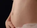 Pancia gonfia e dura, sembro incinta. La pelle liscia e chiara, con un leggero velo di tessuto rosa chiaro.