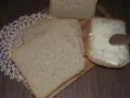 Chleb mieszany pokrojony w kromki, jedna z nich smarowana masłem drewnianą łyżką.