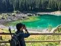 Donna con zaino e macchina fotografica cattura la bellezza del lago di Carezza, in Trentino Alto Adige.
