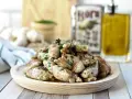 Deliciosas mollejas de cordero salteadas con perejil fresco, servidas en un plato de madera. Al fondo, aceite de oliva y ajos.