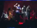 Scena teatralna, gdzie mężczyzna tańczy, a kobiety śpiewają. Atmosfera jak po pożarze w burdelu, pełna emocji i dramatyzmu.