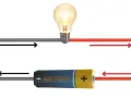 Schemat obwodu elektrycznego z żarówką i baterią. Strzałki pokazują przepływ prądu, ilustrując wzór na napięcie.