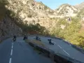 Motociclisti affrontano le curve del Col de Turini, immersi in un paesaggio montano roccioso e verdeggiante.