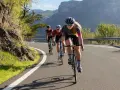 Three cyclists race up a mountain road. The lead cyclist, a woman, is what is a sportive person, focused and determined.