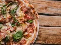 Pyszna pizza carbonara z chrupiącym boczkiem, rukolą i cebulą na drewnianym stole.