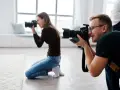 Dwóch fotografów klęczy i robi zdjęcia aparatem w jasnym studiu.