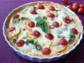 Pyszna tarta na słono z brokułami, pomidorkami koktajlowymi i oliwkami, udekorowana listkiem bazylii.