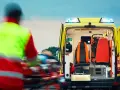 Ratownictwo medyczne w akcji. Ratownik w kamizelce odblaskowej transportuje pacjenta do karetki.