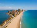 Hohe Gebäude säumen eine lange Sandbucht mit türkisfarbenem Meer und blauer Lagune.