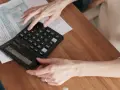 Dłonie liczą na kalkulatorze, przygotowując się do zapłaty rachunków, np. tauron opłata handlowa.