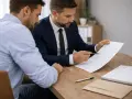Mężczyzna w garniturze wskazuje na dokument, omawiając propozycję ugody wzór z klientem.