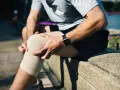 Mężczyzna z bólem kolana, bandaż na nodze, próbuje wykonać przeprost kolana.