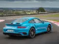 Błękitne Porsche 911 Turbo S na torze wyścigowym, z widokiem na miasto w tle.