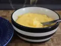 En skål med krämig, gul lemon curd, redo att bredas på en blå tallrik.