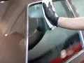 Ręka w czarnej rękawiczce czyści szybę samochodu białą ściereczką.