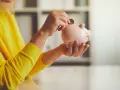Persona con suéter amarillo deposita moneda en hucha. Un asesor fiscal te ayuda a ahorrar.
