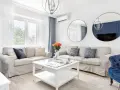 Jasny salon w stylu hampton z beżowymi sofami, białym stolikiem kawowym i niebieskimi akcentami.