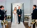 Panna młoda w sukni ślubnej idzie z ojcem do ołtarza, obok bukiety kwiatów.