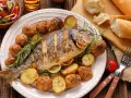 Pieczona ryba z ziemniakami, cytryną i rozmarynem na talerzu.