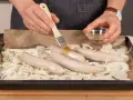Bratwurst im Backofen: Zwiebelringe auf Backpapier, darauf vier rohe Bratwürste. Mit einem Pinsel wird Öl aufgetragen.
