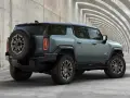 Zielony hummer elektryczny z kołem zapasowym z tyłu, zaparkowany przy betonowej konstrukcji z łukami.