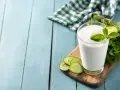Szklanka białego napoju, idealna na kefir w ciąży, ozdobiona plasterkami ogórka i miętą.
