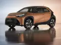 Brązowy Toyota Aygo X z czarnym dachem i felgami na błyszczącym podłożu.