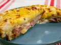 Croque Monsieur gratinado con queso derretido y jamón, servido en plato azul.