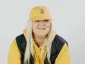 Frau mit gelber Kappe und Kapuzenpullover lächelt.