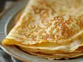 Pile de crêpes dorées sur une assiette, parfaites pour une recette crêpe 6 personnes.