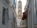 Wąska uliczka w Tunezji z wieżą w tle. Czy do Tunezji potrzebny jest paszport? Tak, do podróży do Tunezji potrzebny jest paszport.